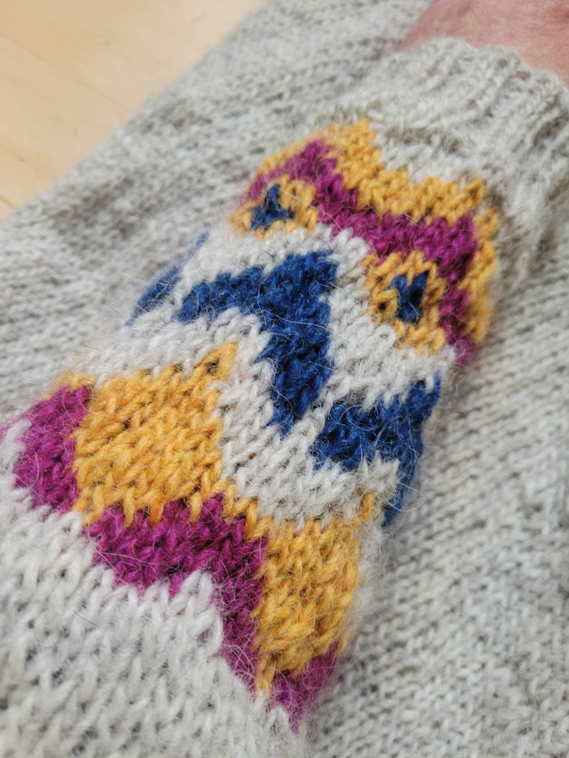 Schräge Detailaufnahme der Maschenstruktur eines handgestrickten Islandpullovers „Loimüneule“ aus 100 % Léttlopi-Wolle mit farbigem Rundpassenmuster in Blau, Senfgelb und Beere.
