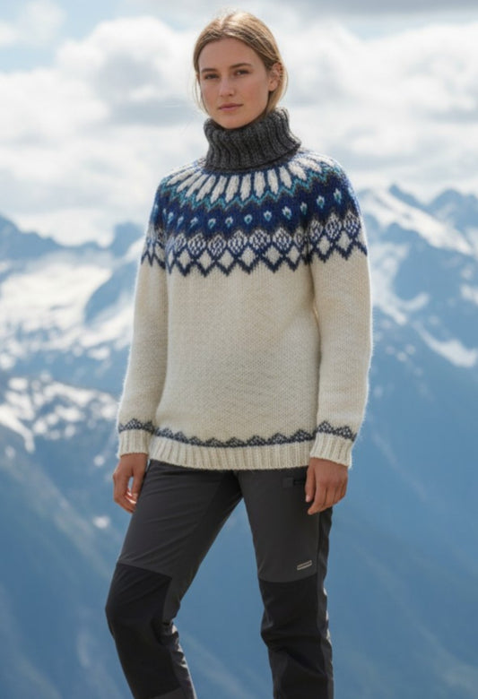 Handgestrickter Islandpullover Alfheidur Nordic Sea Größe M aus Lettlopi Wolle in Naturweiß mit blauem Rundpassenmuster vor Bergkulisse