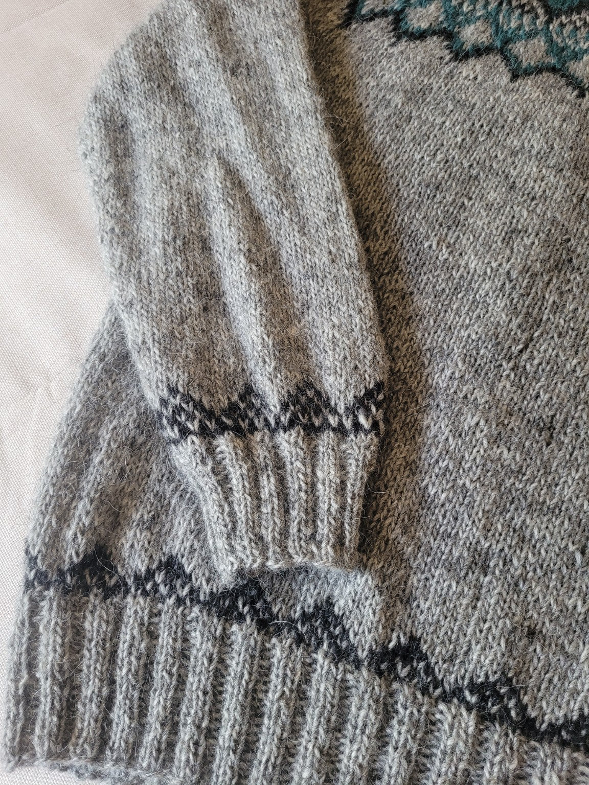 Detail des Ärmelbündchens vom handgestrickten Islandpullover Alfheidur Nordic Sea mit nordischem Jacquardmuster.