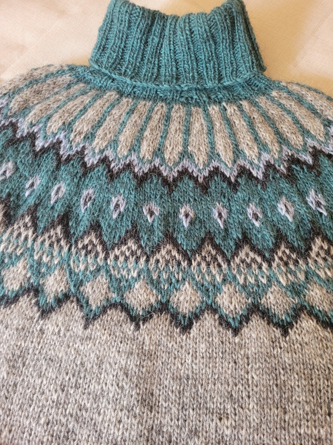 Detail der handgestrickten Rundpasse des Islandpullovers Alfheidur Nordic Sea mit isländischem Strickmuster in Petrol, Grau und Naturweiß.
