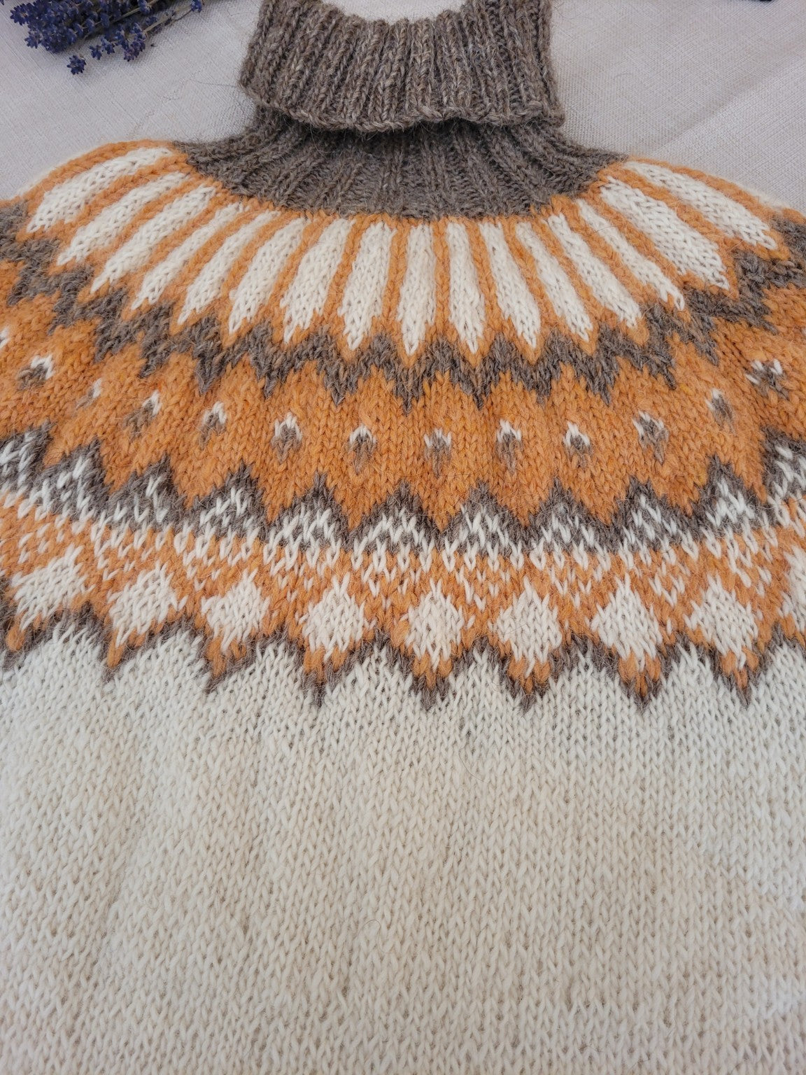 Detail der nordischen Rundpasse des handgestrickten Islandpullovers Alfheidur Winter Light in Naturweiß, Ocker und Taupe.