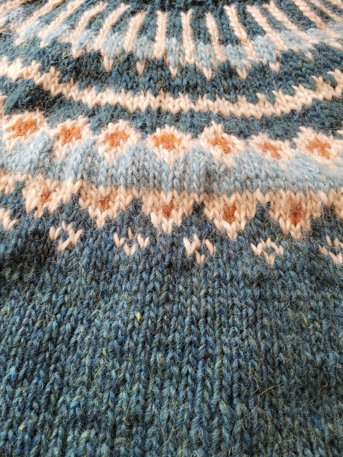 Detailaufnahme des nordischen Musters eines handgestrickten Islandpullovers aus Álafosslopi Wolle in Petrol, Eisblau, Naturweiß und Rost.