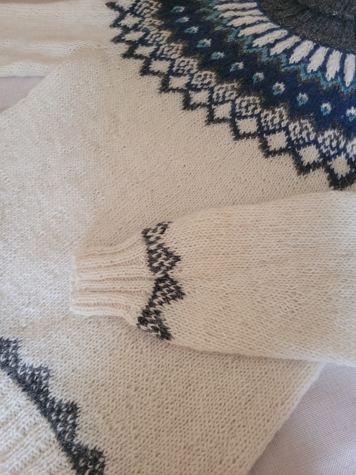 Detailaufnahme des Ärmelbündchens eines handgestrickten Islandpullovers aus echter isländischer Lettlopi-Wolle mit traditionellem isländischem Muster.