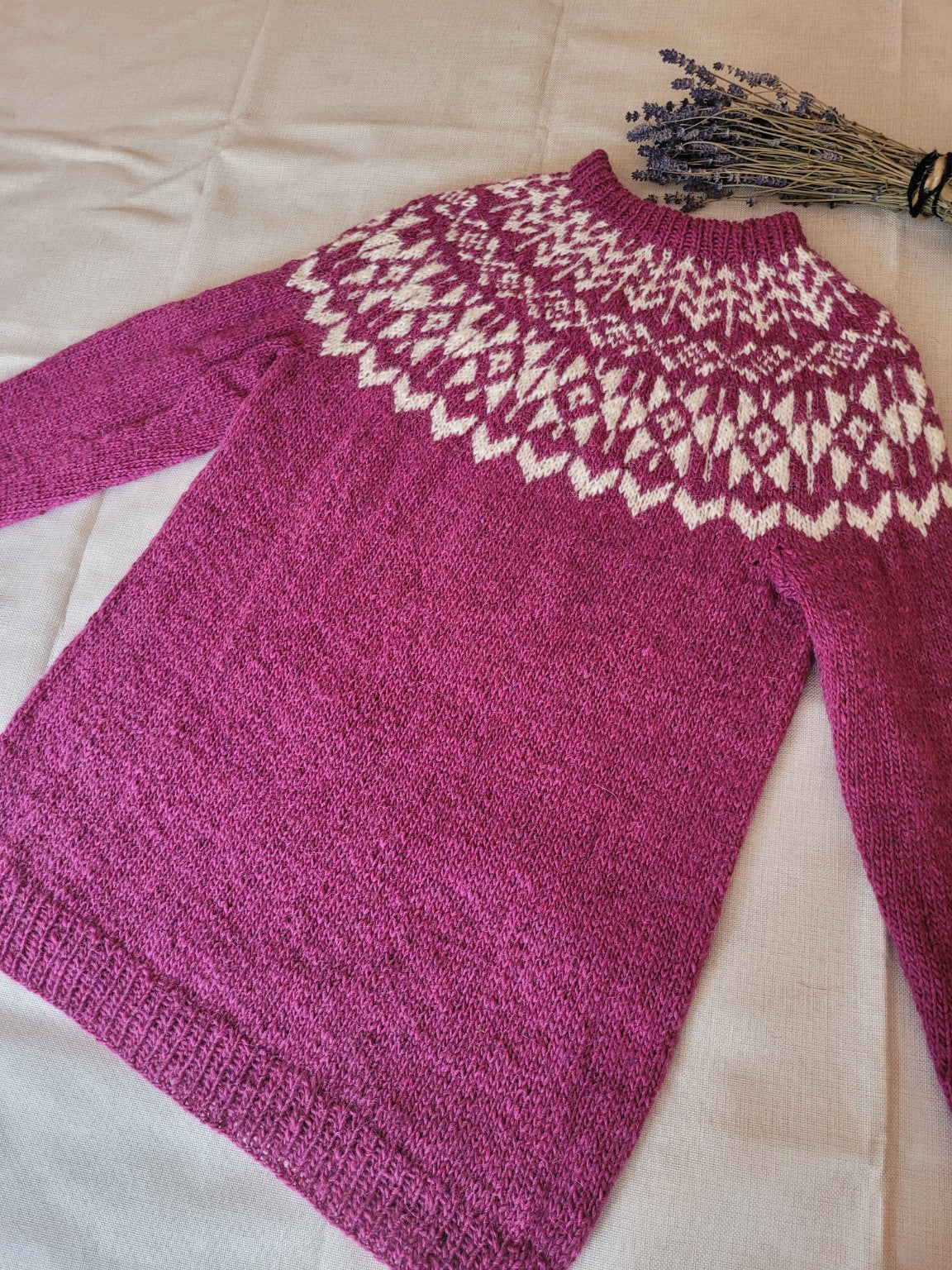 „Hellargjá Islandpullover aus Léttlopi mit handgestrickter Rundpasse in Beere und Naturweiß, flach liegend“