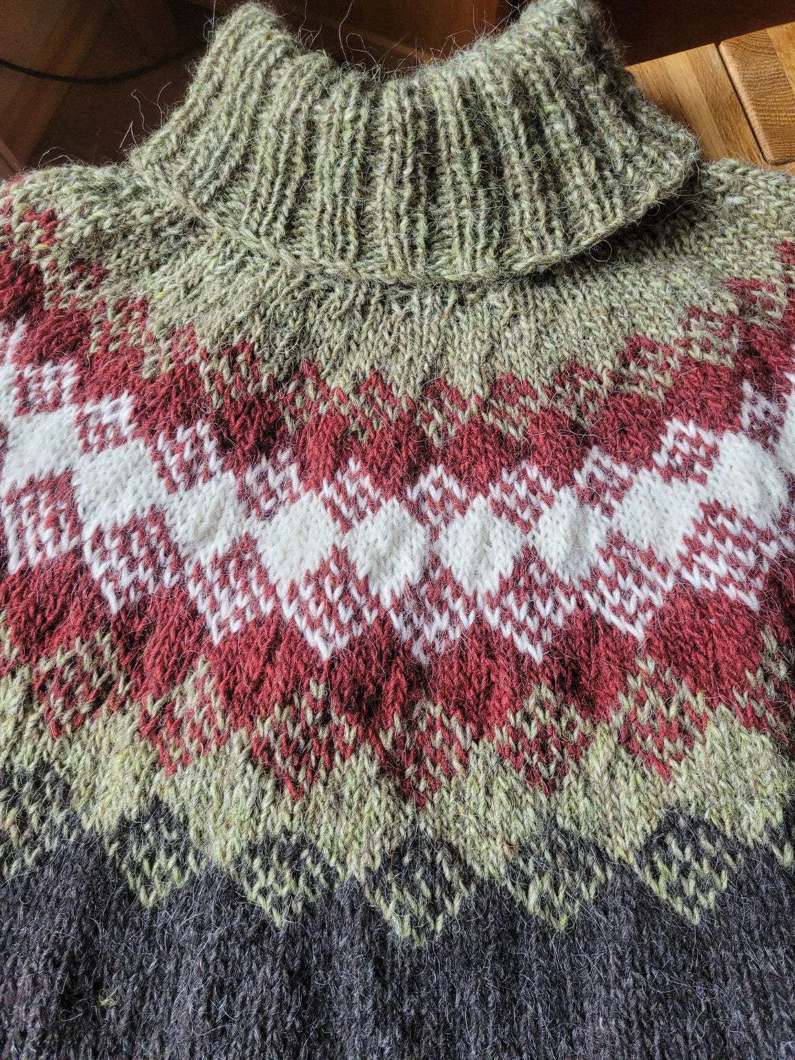 Detailaufnahme des Rollkragens und des nordischen Jochmusters in Rostrot, Creme und Salbeigrün bei einem handgestrickten Islandpullover aus Lettlopi.