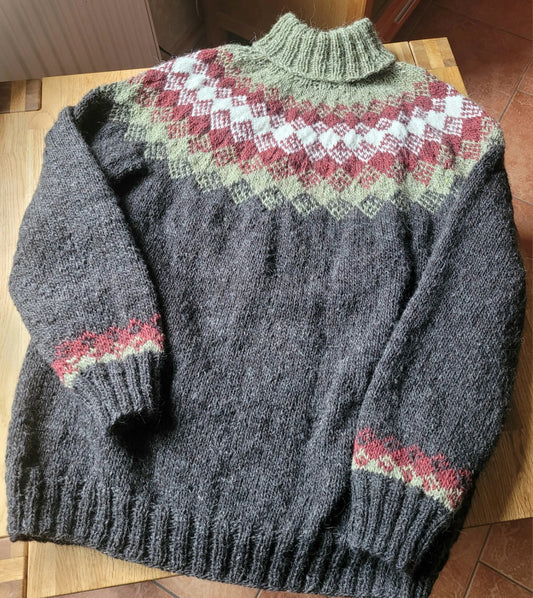 Handgestrickter Islandpullover „Hiutaleneule“ aus Lettlopi in Anthrazit mit nordischem Jochmuster in Rostrot, Creme und Salbei, flach auf einem Holztisch liegend.
