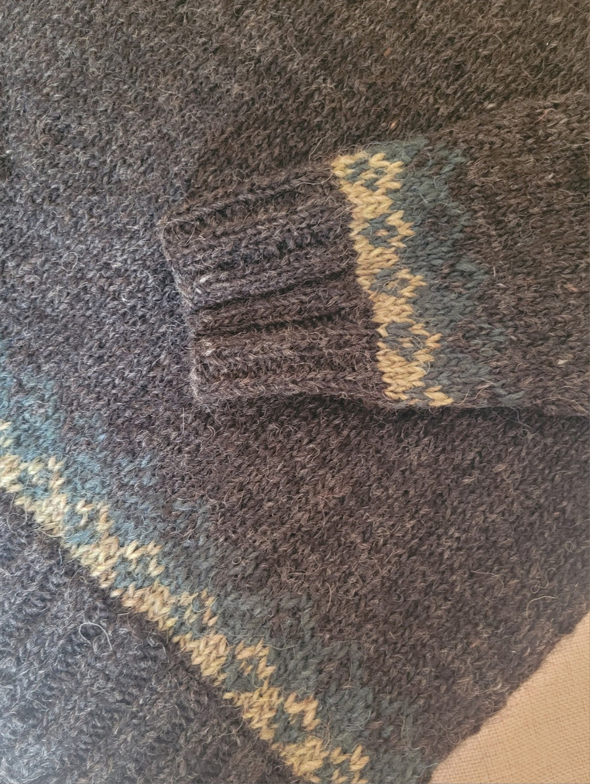Detailaufnahme des Ärmelbündchens eines handgestrickten Islandpullovers aus isländischer Lettlopi-Wolle in Anthrazit, Moosgrün und Naturweiß.
