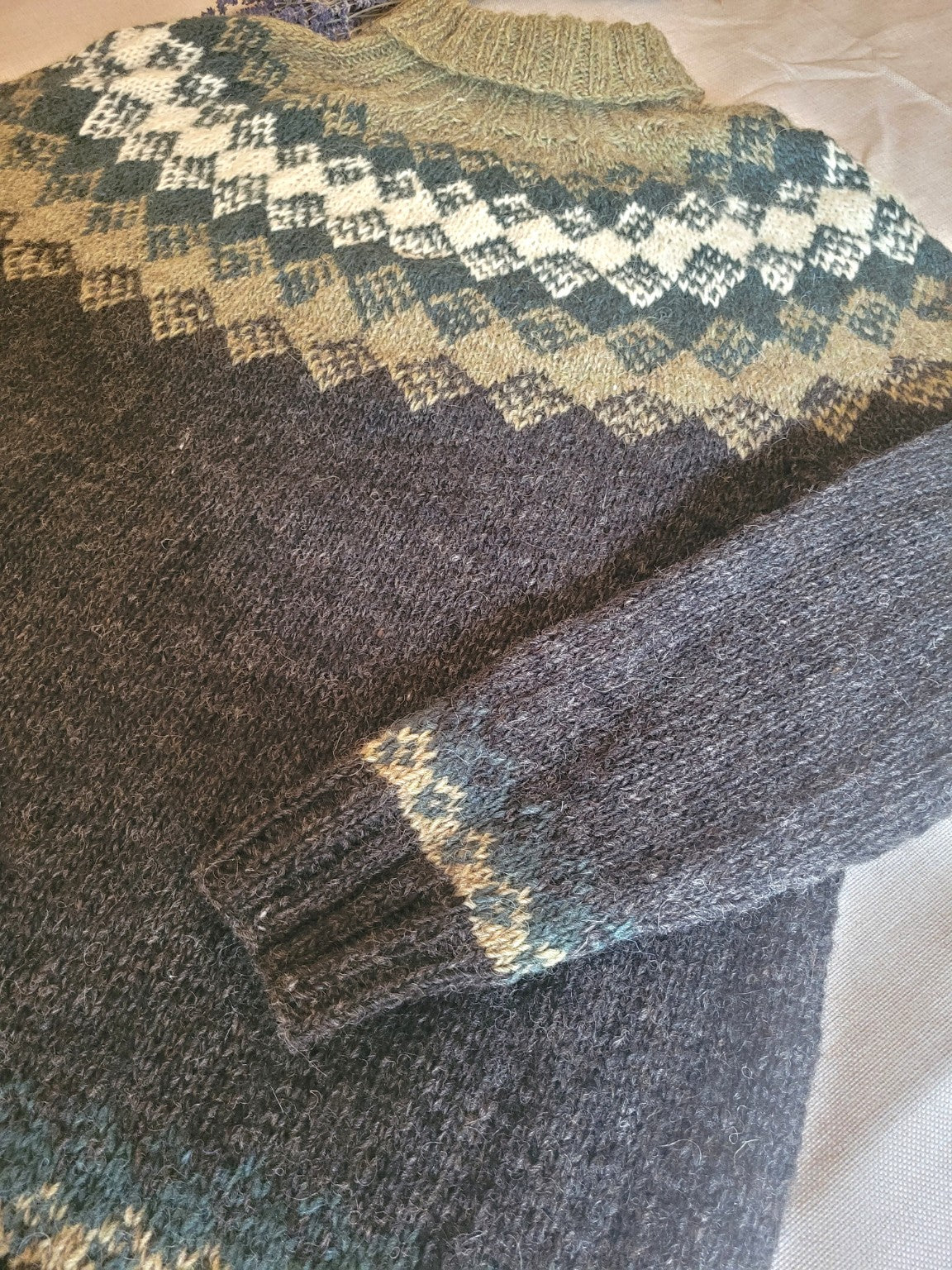 Detailaufnahme der traditionellen Rundpasse und des Ärmelmusters eines handgestrickten Islandpullovers aus echter isländischer Lettlopi-Wolle.