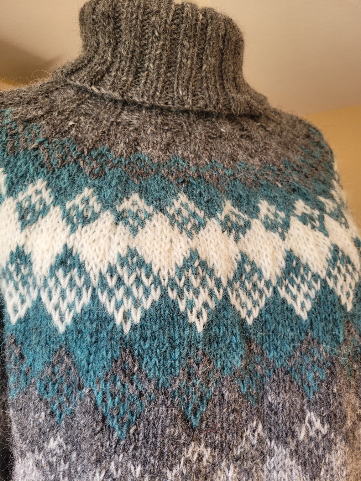 Detailaufnahme des handgestrickten nordischen Musters aus Islandwolle in Grau, Petrol und Naturweiß mit weicher Wollstruktur.
